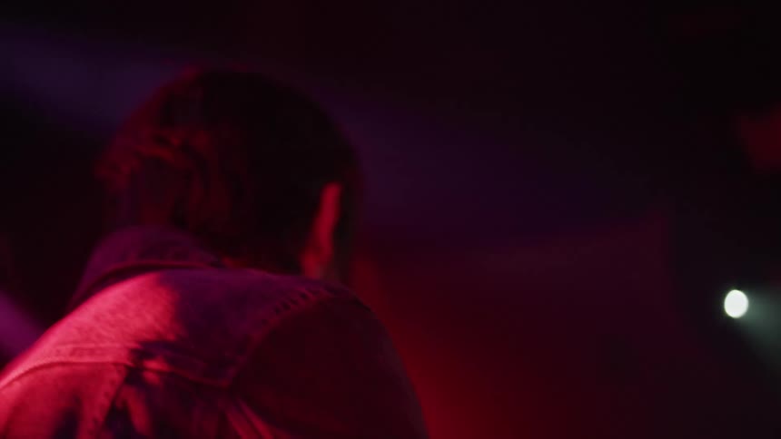 A drummer in a denim jacket plays at a venue with his band