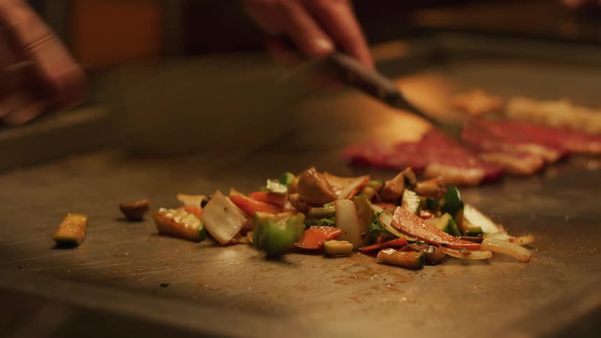 A person in a room cooking vegetables and meat on a grill with utensils