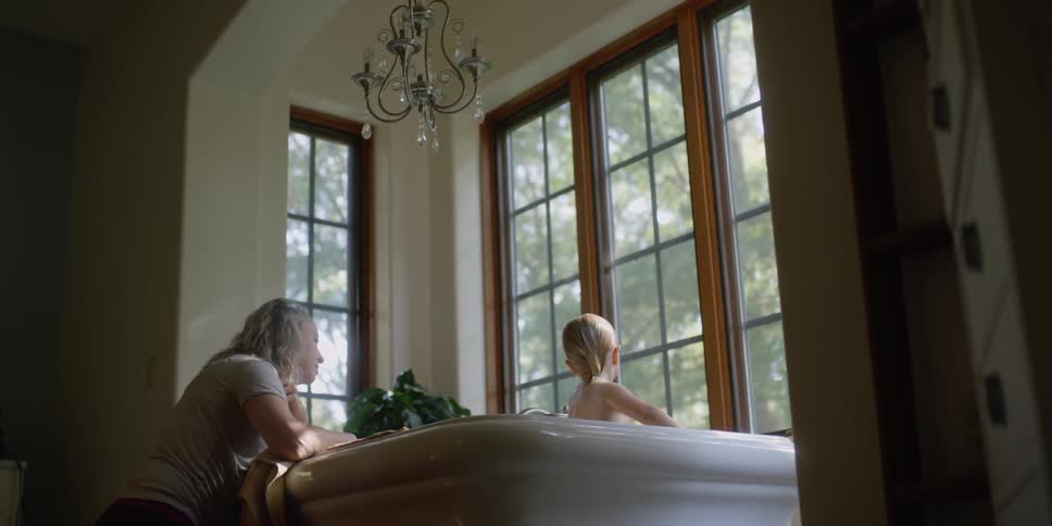 A toddler taking a bath while his mother supervises