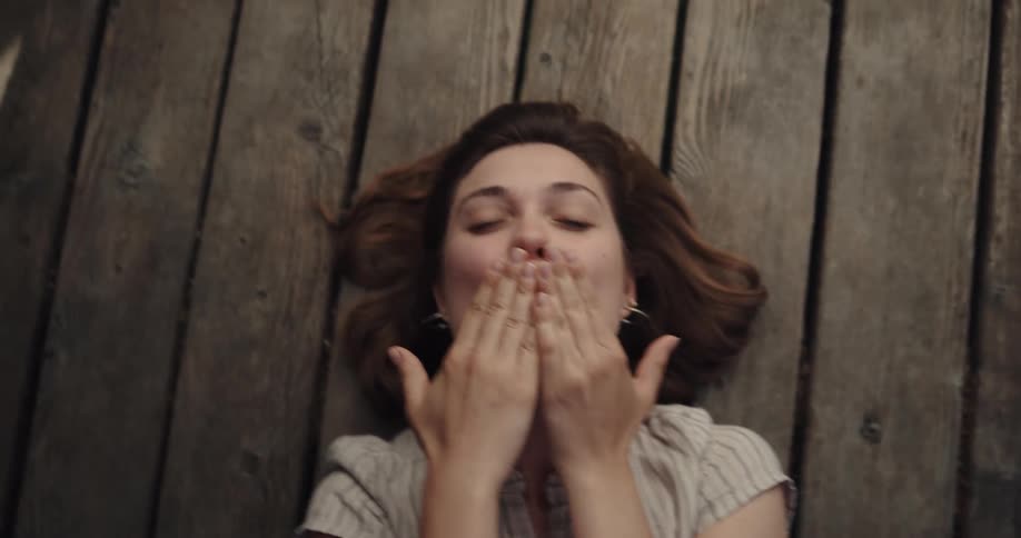 A woman smiling and blowing kisses while lying on wood planks