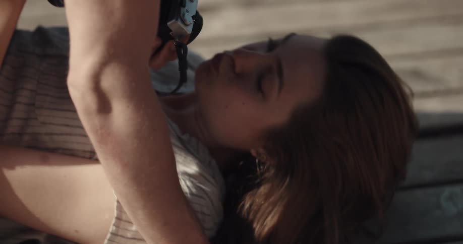 Man takes pictures of woman lying on pier near rippling lake before leaning down to kiss her