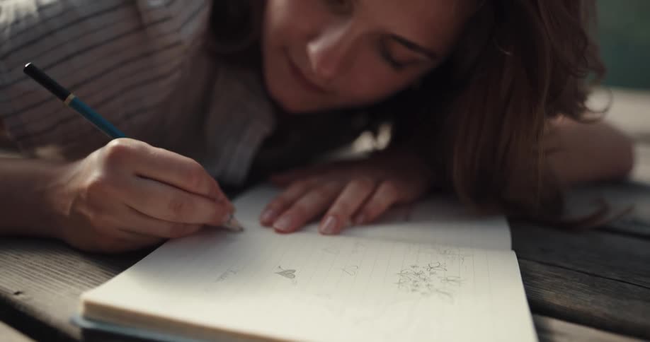 A teenage girl doodling in a notebook while lying on her stomach