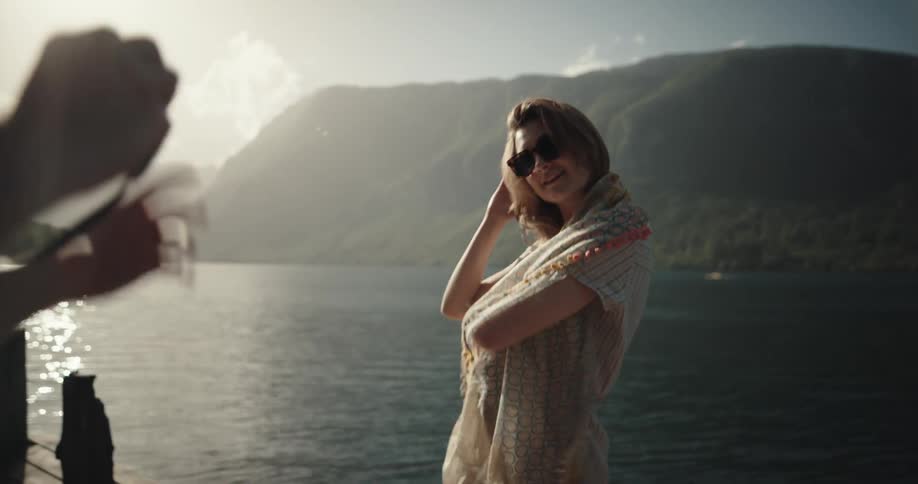 A woman poses with a scarf on a pier while a man directs her and takes photographs