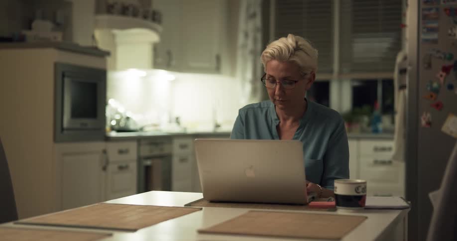 A woman sits at her kitchen table and uses her laptop