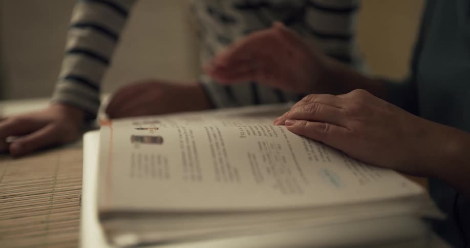 An adult and a child reading a book over a table