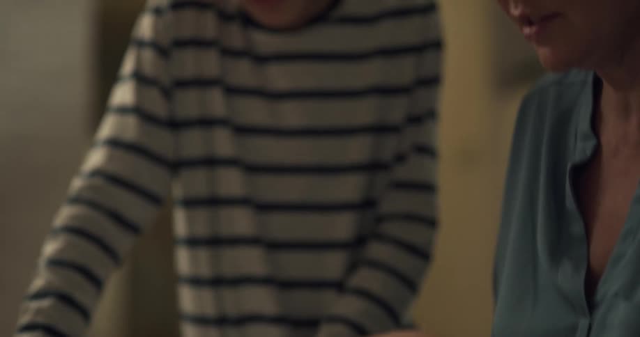 A woman helps her son with homework by pointing out a passage in a textbook