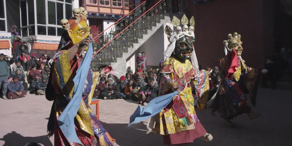 People wearing masks and colorful costumes dancing on a street in front of a crowd