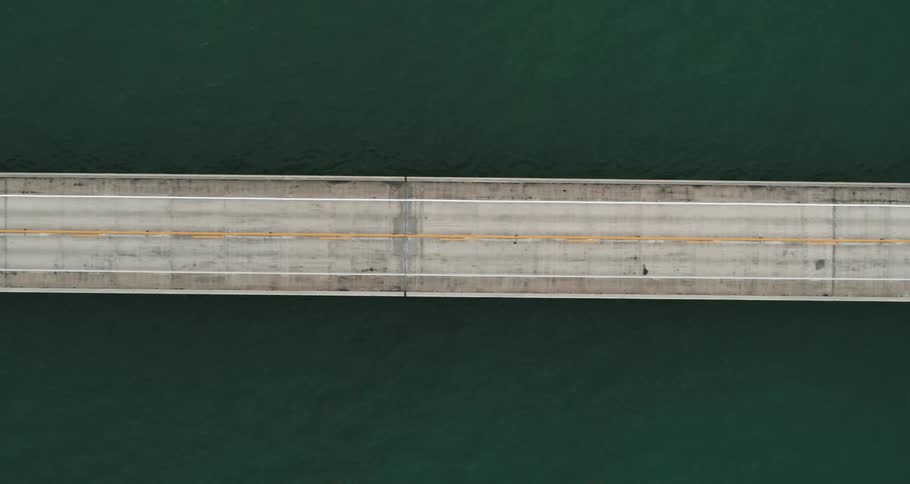 Aerial view of light traffic on a bridge surrounded by water