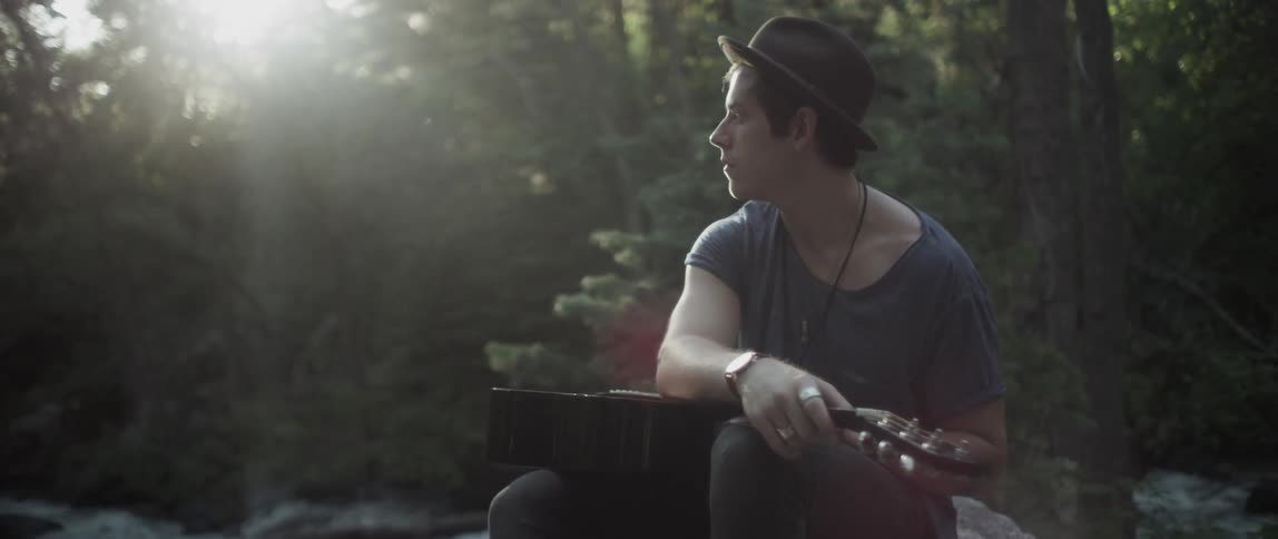 A man has a guitar on his lap as he looks to the side