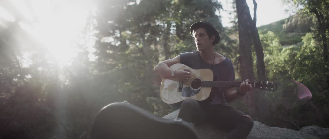 A man plays guitar while sitting in the wilderness