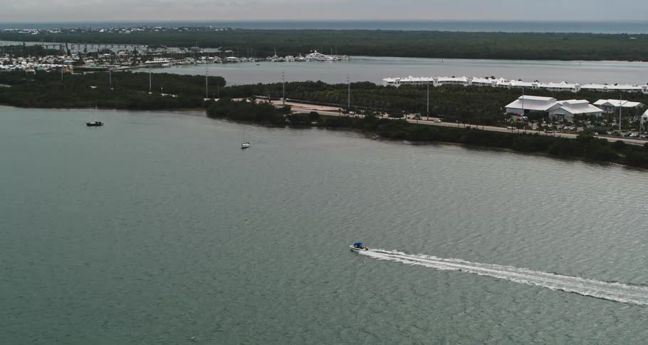 A boat speeds across the water leaving a wake as it goes along a coast