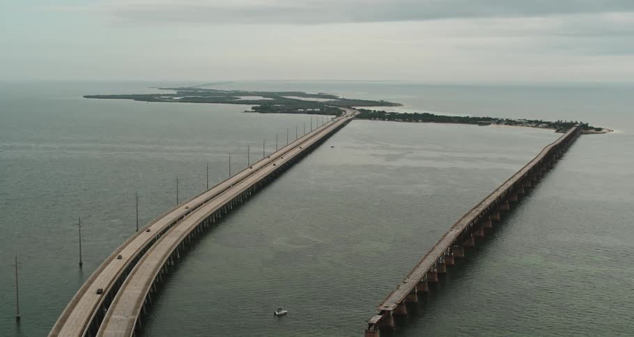 Traffic flows along road crossing ocean water to islands near misty horizon under cloudy sky