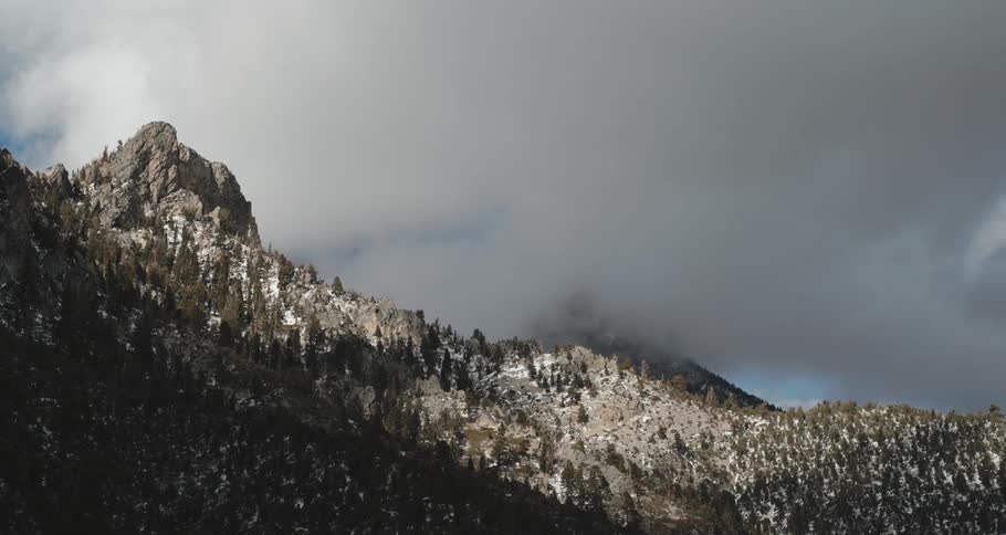 A mountain summit in a forest with a slope and a large cloudy overcast during the day