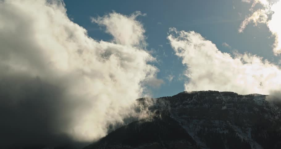 Thick clouds loom over a mountain ridge on a sunny day