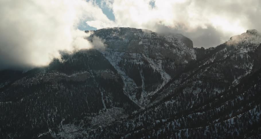 Sunlight peaks through dense clouds over snow capped mountains