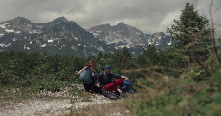 Hikers sit on ground resting with mist obscuring snow dotted mountains in background under over cast sky