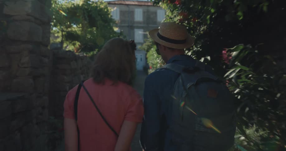 A man and woman traveling walk down a pathway and talk as the woman pulls her luggage behind her
