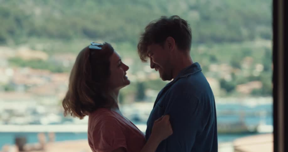 A man and woman stand looking over a port and kiss