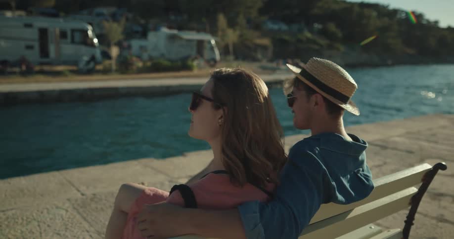 Young couple on vacation sitting on a bench in the pier at morning
