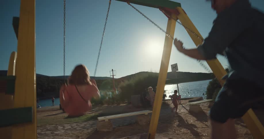 A man and woman swing on a small swing set by a lake