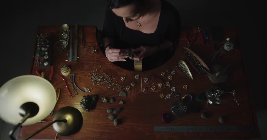 A woman sitting at a table putting together a soldering iron to make jewelry
