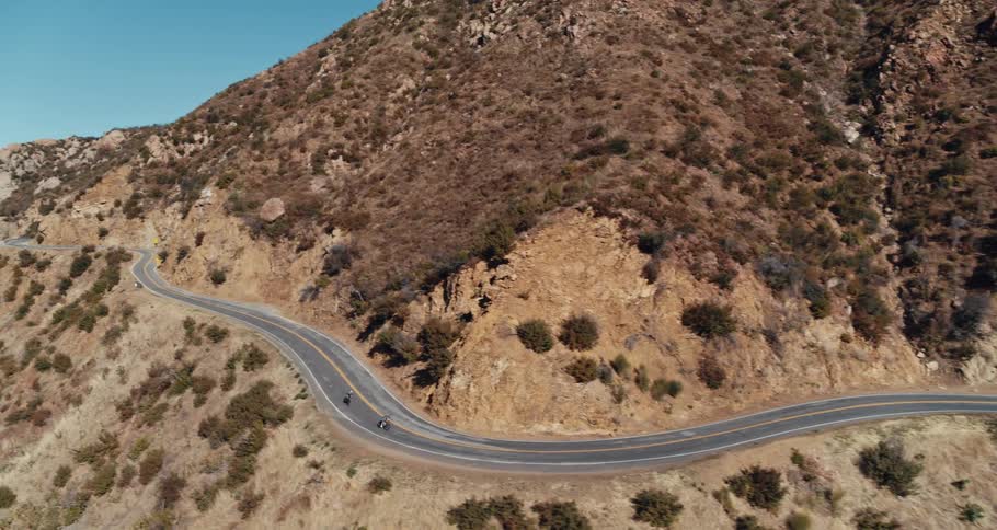 Two bicyclists ride their bikes on a highway through the mountains