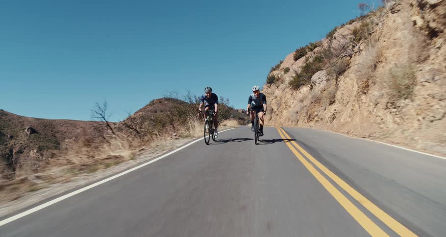 Two men cycle down a mountain road