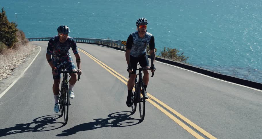 Two men cycle up a road next to the ocean