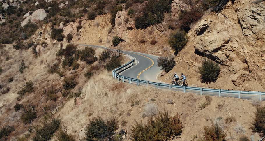 Two people are riding bicycles on a mountain road