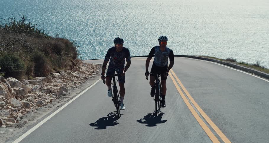 Two bicyclists ride on a highway near the ocean