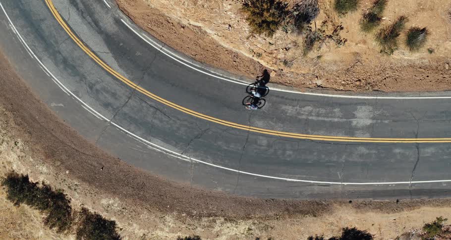 Two people riding bicycles on the highway near plants and dirt