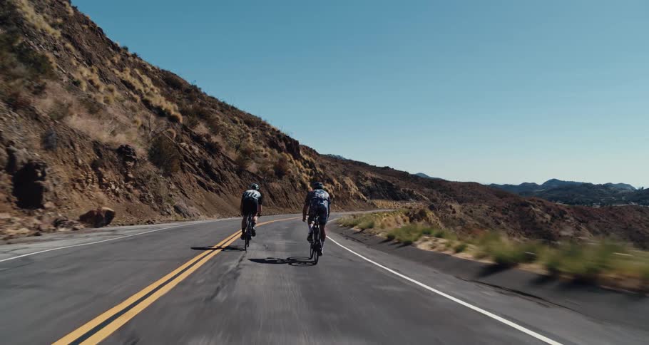 Two bicyclists ride along the edge of a curved road on a steep slope