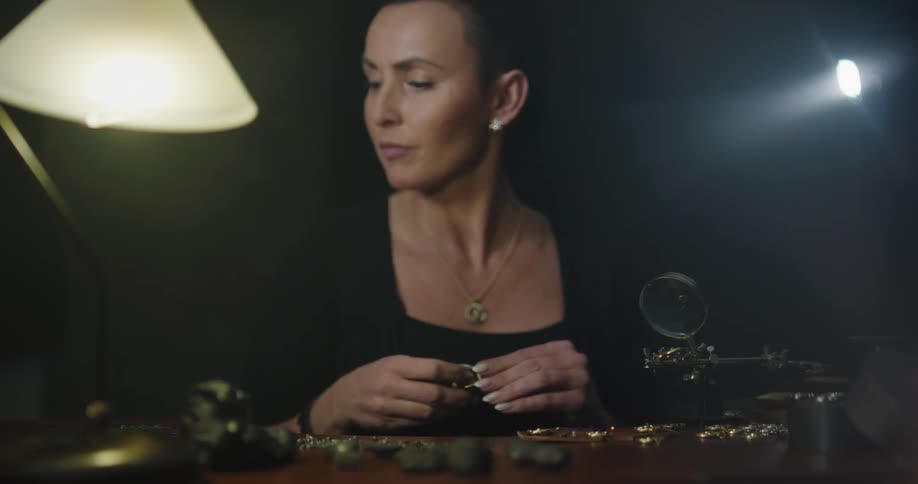 Woman wearing a necklace examines jewelry with a jewelers eye loupe then reaches for a wrench