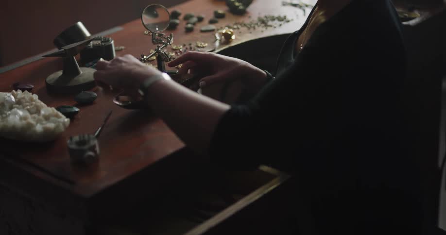 A woman is grabbing jewelry making tools from her desk