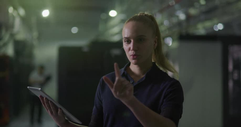 Woman with a pony tail holds a tablet with one hand and taps and swipes in the air with her other hand