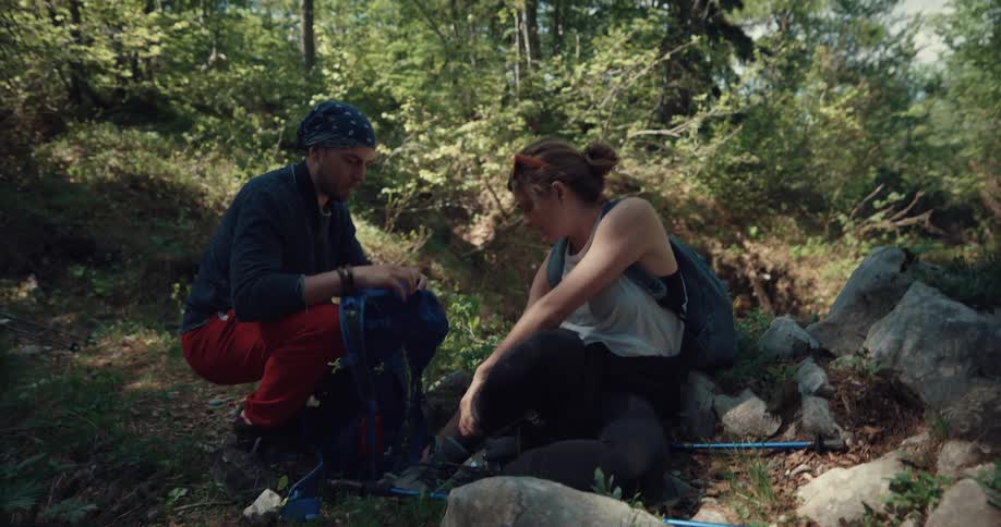 A female hiker sits and holds her injured ankle while her male companion tends to her