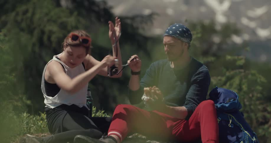 A couple play around as they stop backpackaging to eat near mountains