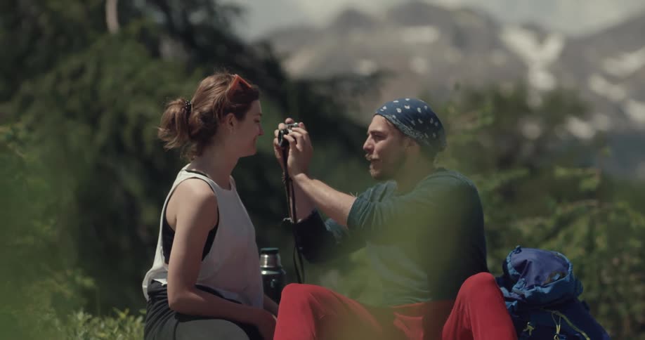 A man sits up on the mountain and takes a picture of a woman
