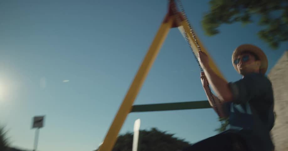 Man and woman swing on swing set with lake or brick wall on opposite ends of the arc