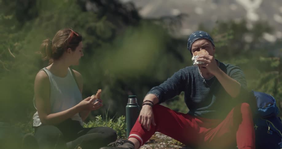 A man and woman eating sandwiches while hiking in a forest