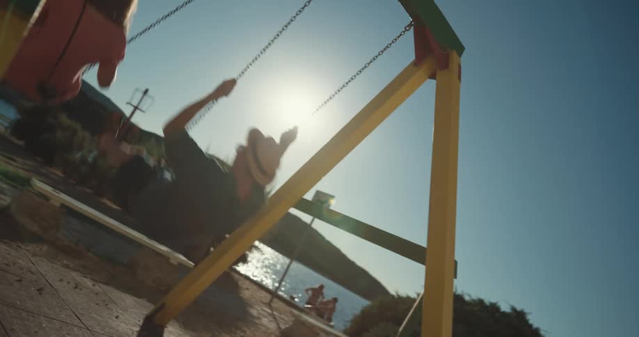 A man and woman swing on a swing set near the beach on a sunny day