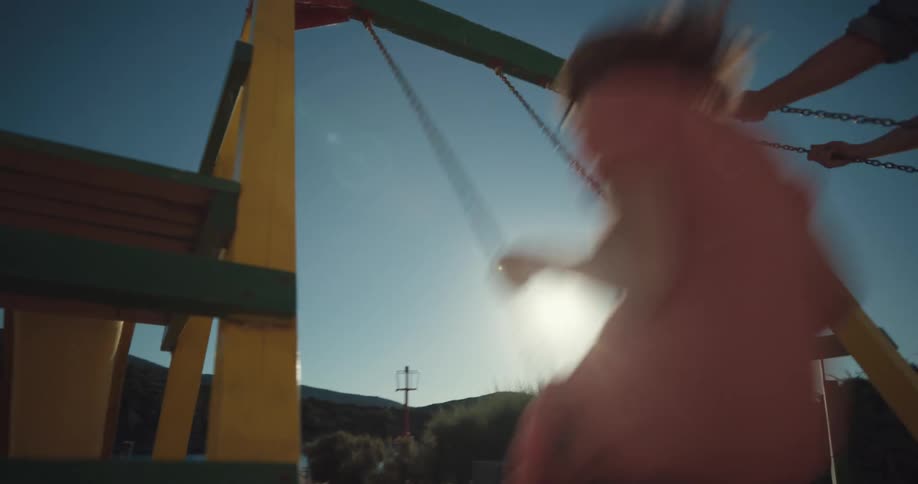 A man and woman ride swings at a playground near a lake