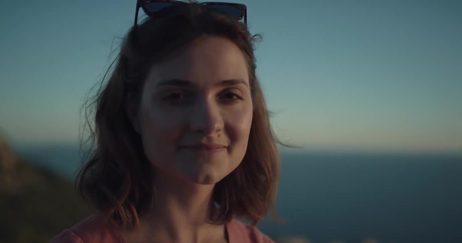 A woman standing overlooking the ocean turns her head and smiles