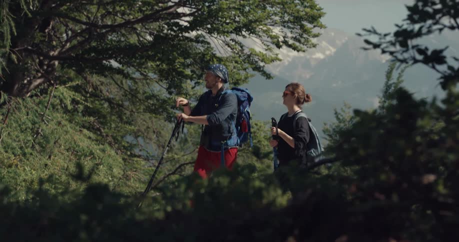 A man and woman in a forest hiking with trees the sky and clouds in the background
