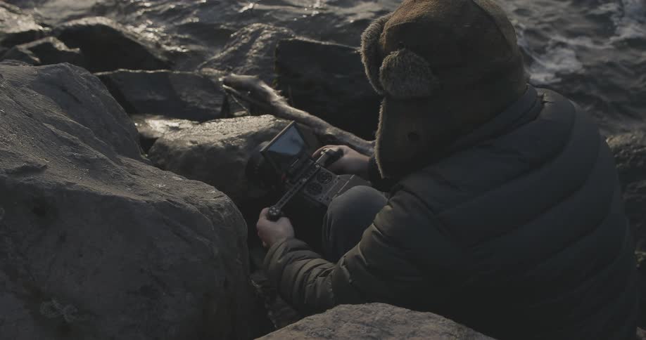 A man sits on rocks very close to the water taking photographs
