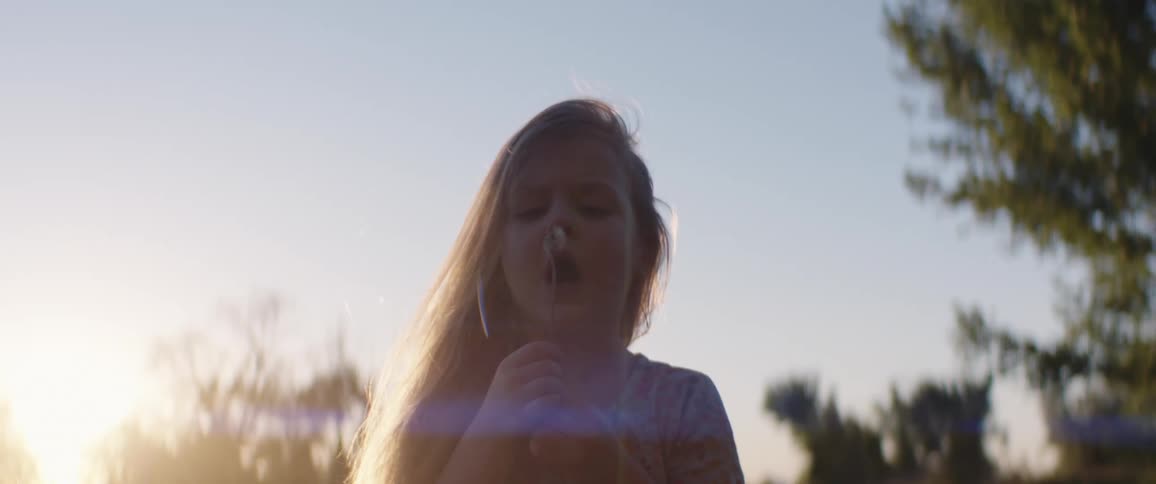 Child blowing on a dandelion in the summer