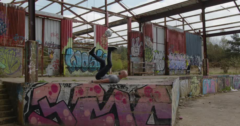 A man lays on his back and juggles a soccer ball with his feet