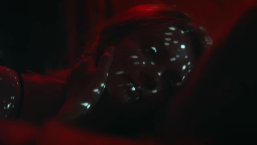 A female lays on her side as lights are projected onto her face in the darkness