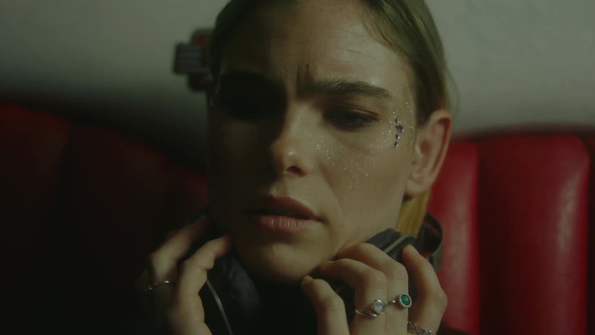 A woman slowly removes a set of headphones while she has an unsettled expression upon her face