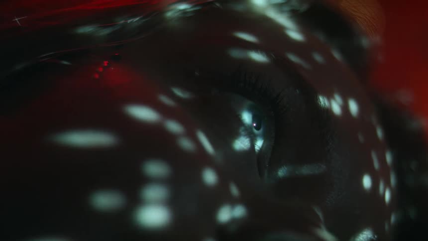 White dots of light flow across face of staring woman lying on side against orange background